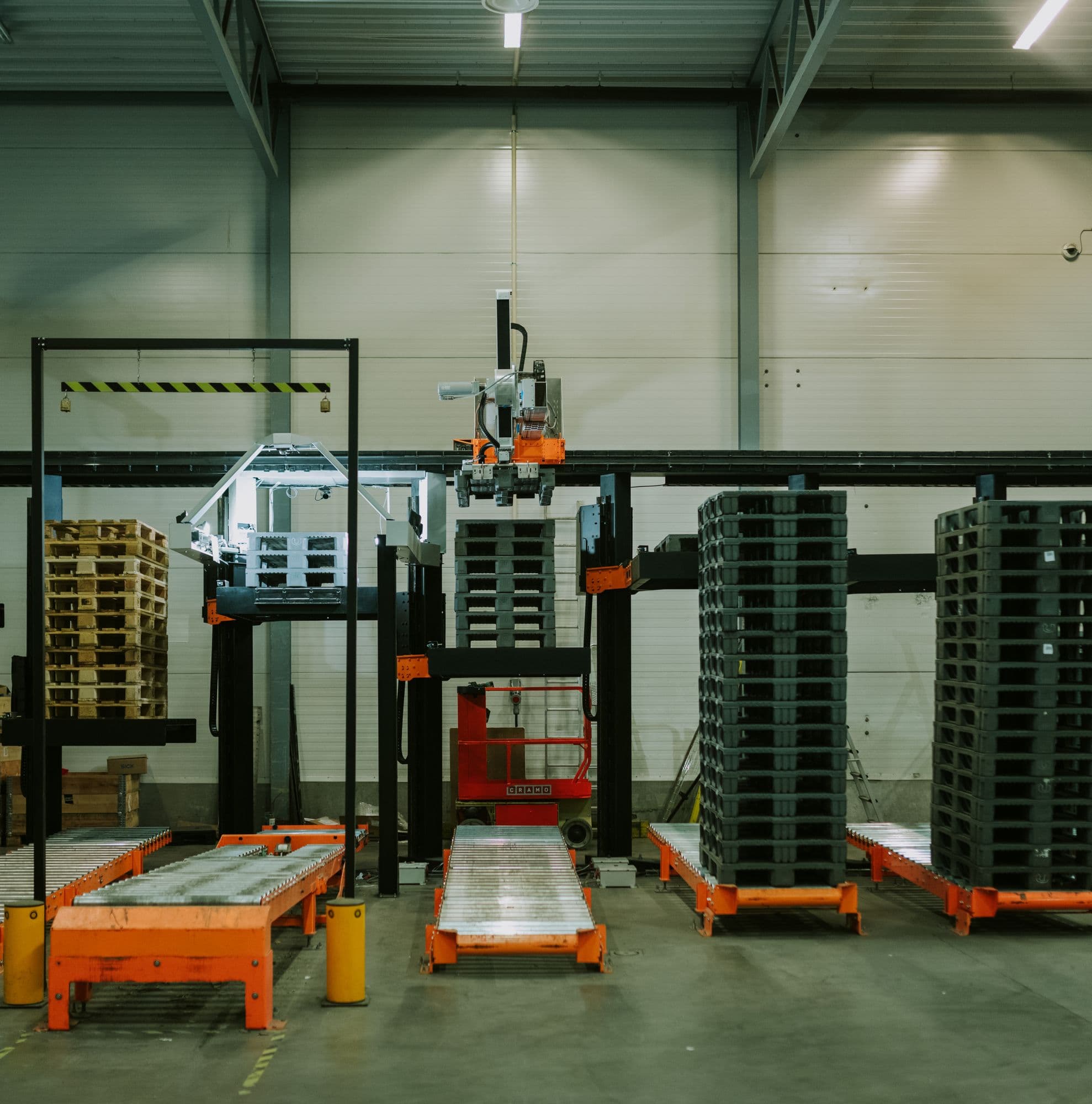 A dimly lit warehouse filled with pallets and a robotic arm sorting them