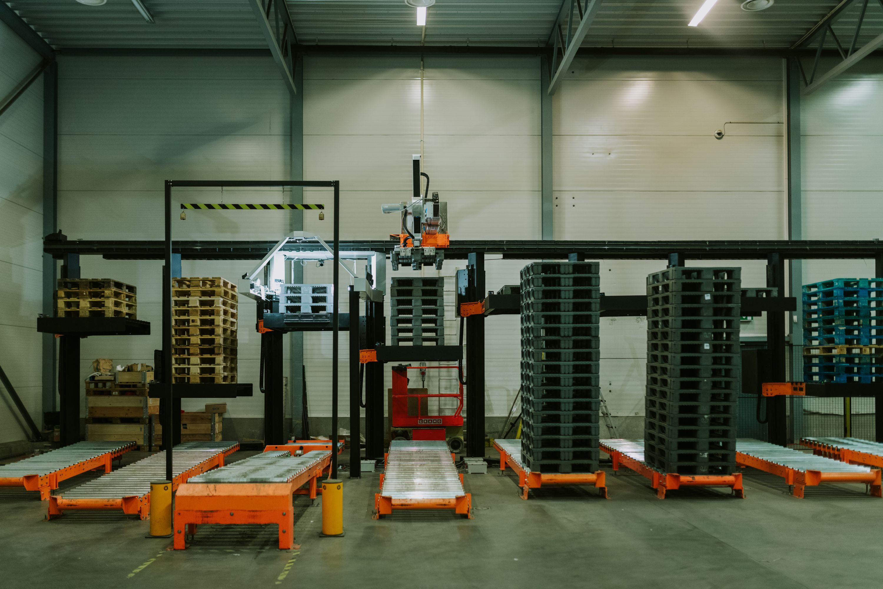 A dimly lit warehouse filled with pallets and Solwr's robotic arm sorting them